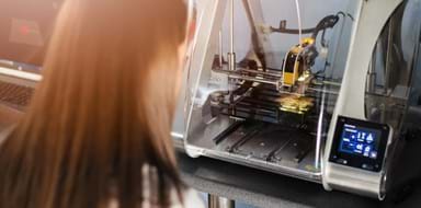 Young woman in white lab coat working with 3d printer