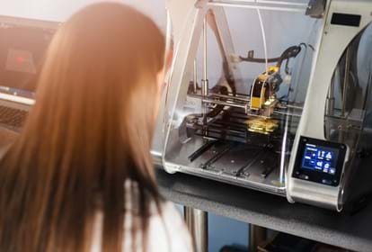 Young woman in white lab coat working with 3d printer