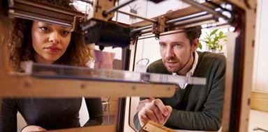 Two Designers Working With 3D Printer In Design Studio