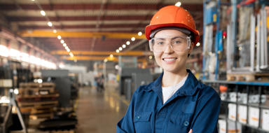 Young smiling female technician in blue uniform, protective eyeglasses and helmet working in modern factory