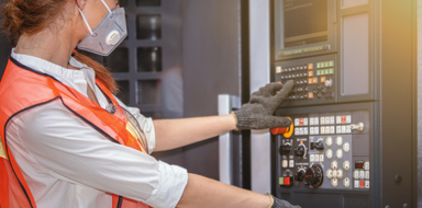Young woman engineer protecting herself with a face mask operating a machine inside a factory