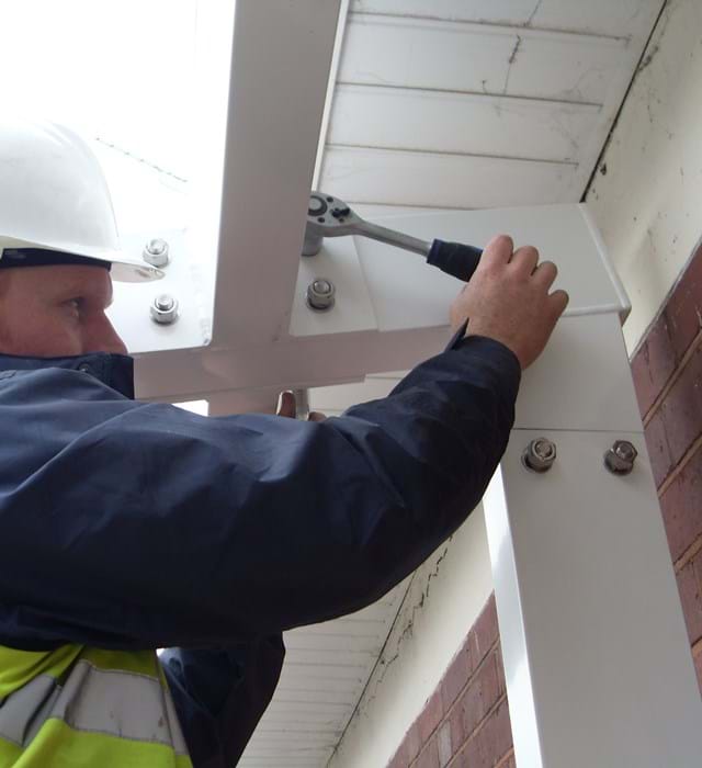 Twinfix staff member in a hard hat tightening bolts on a building