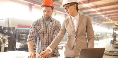 Young technical professionals pointing at sketch on paper while standing by table and discussing blueprint