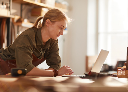 Warm toned portrait of successful female artisan using laptop in crafting workshop