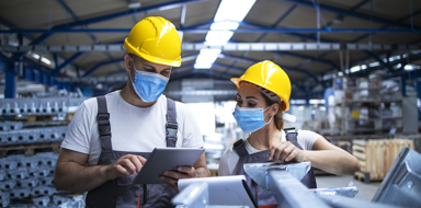 Industrial workers with face masks protected against corona virus discussing about production in factory. People working during COVID-19 pandemic.