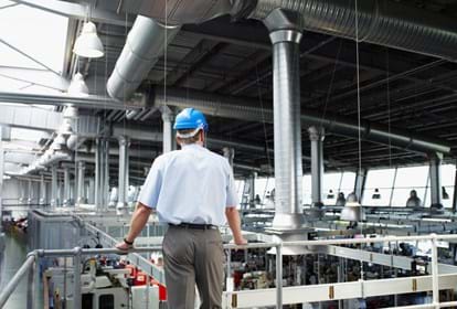 Businessman in hard-hat looking at factory floor from behind