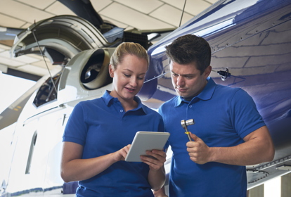 Aerospace Engineers Working On Helicopter In Hangar Looking At Digital Tablet