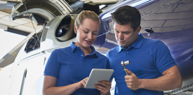 Aerospace Engineers Working On Helicopter In Hangar Looking At Digital Tablet