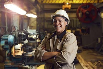 Waist up portrait of female worker posing confidently while standing with arms crossed in factory workshop