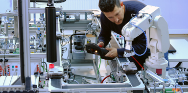 An engineer is programming robotic arm with control panel (teach pendant) which is working on smart factory production line