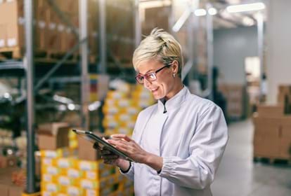 Blonde woman in white uniform using tablet in warehouse