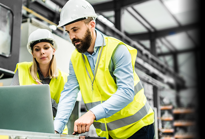 Two manufacturers stood inside an industrial factory looking at a laptop.